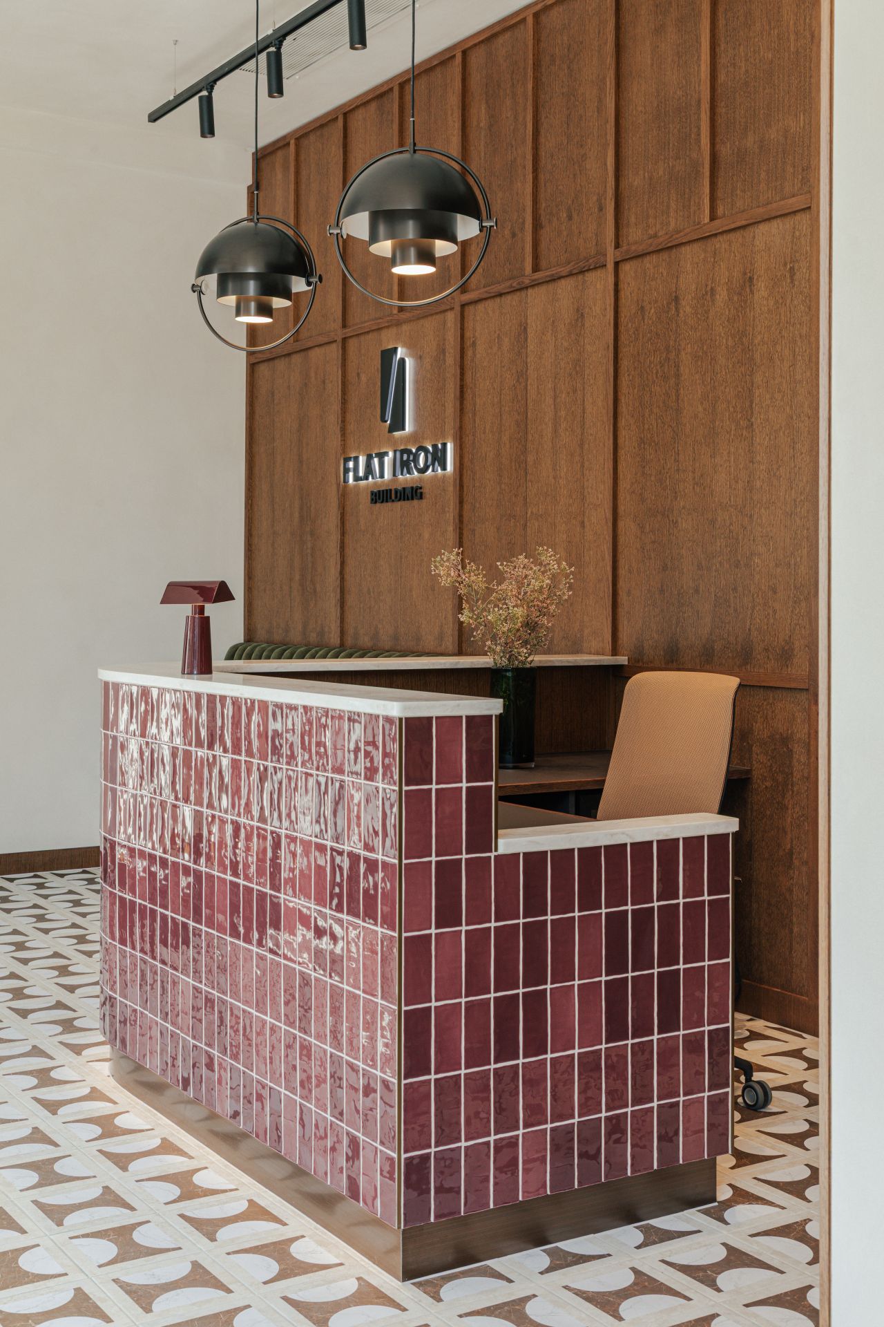 Reception desk with red tiles and patterned floor in a modern office lobby.