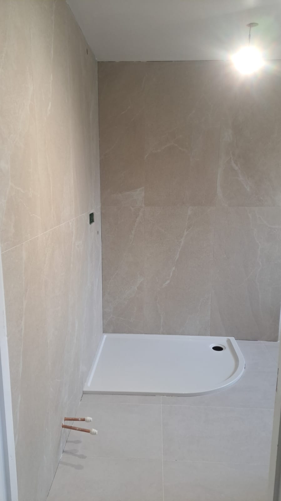 Empty shower space with beige tiles and a white shower tray under a ceiling light.