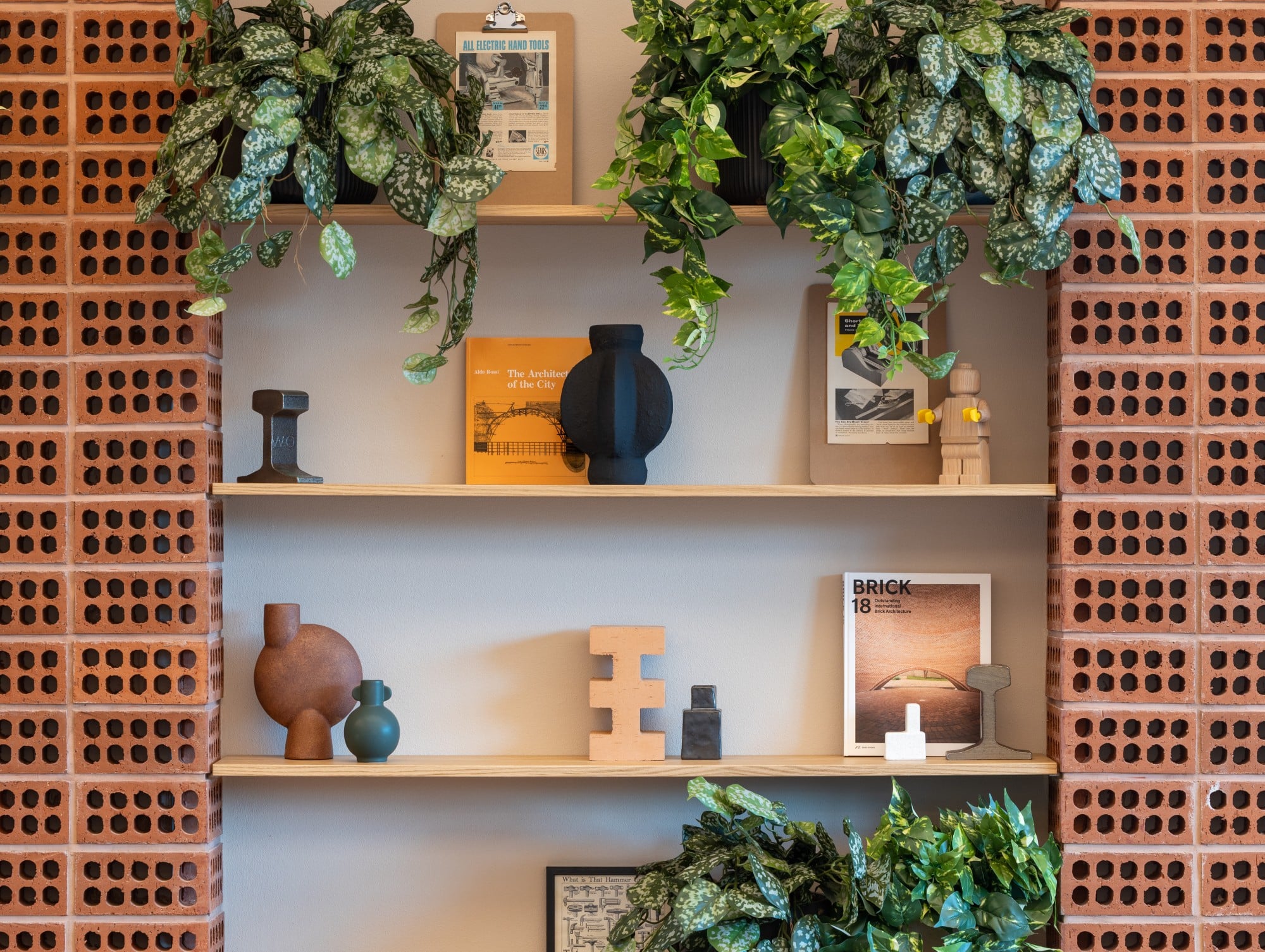 Shelves with plants, books, vases, and art against a wall with a brick pattern.
