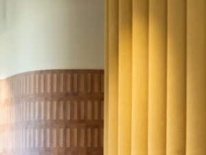 Close-up of yellow vertical blinds with patterned wall in the background.