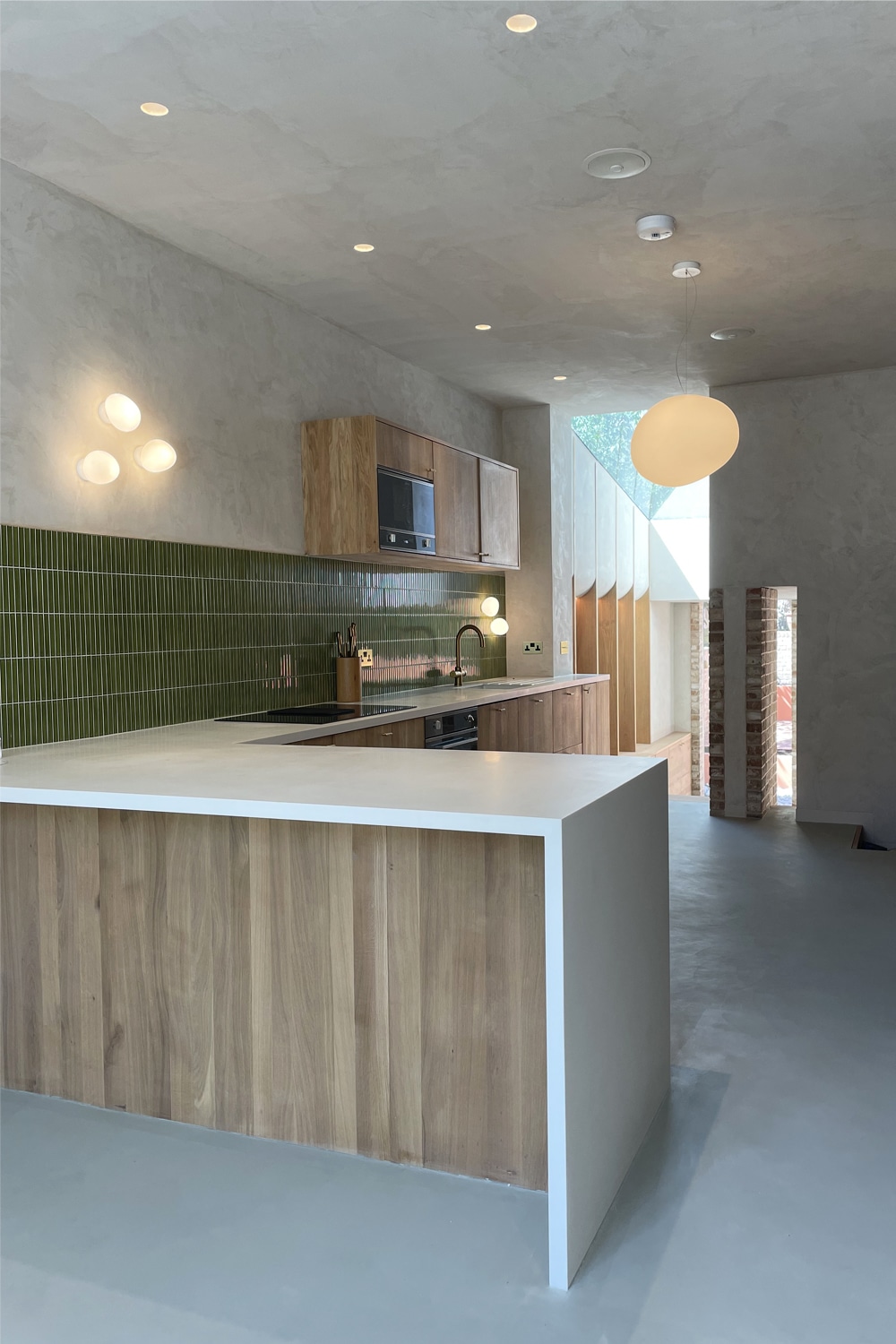 Modern kitchen with wood cabinets, white countertops, and a green tile backsplash.