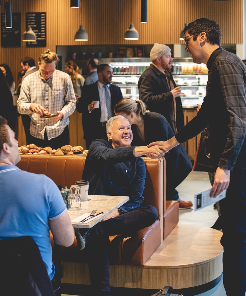 People socializing and shaking hands in a busy café or restaurant setting.