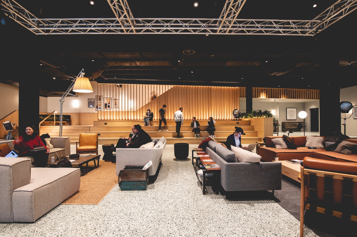 Modern lounge with sofas and people working and socializing in an open, well-lit space.