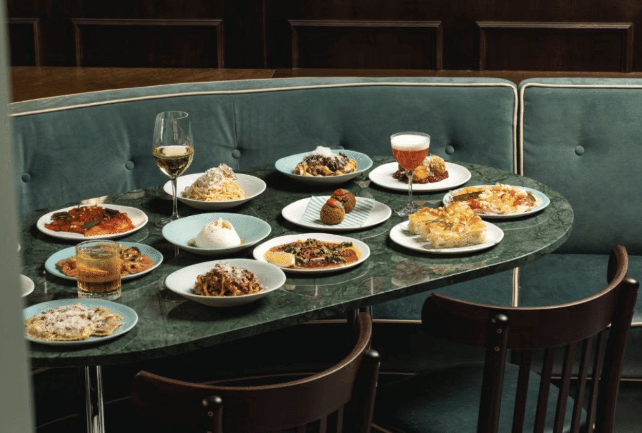 A table with plates of Italian food and drinks in a restaurant booth.