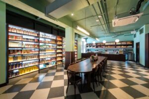 A modern restaurant interior with checkered floors, long table, and shelves filled with food items.