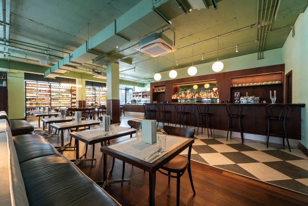 Modern restaurant interior with tables, chairs, booth seating, and a bar area under ambient lighting.