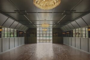 Empty room with wooden floors, large windows, and chandeliers hanging from the ceiling.