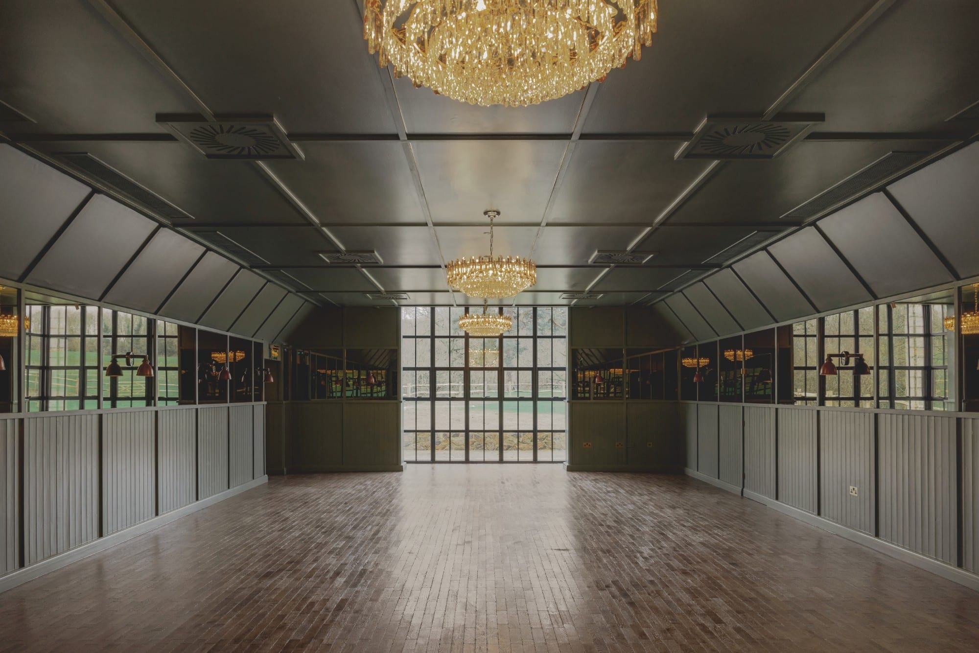Empty room with wooden floors, large windows, and chandeliers hanging from the ceiling.