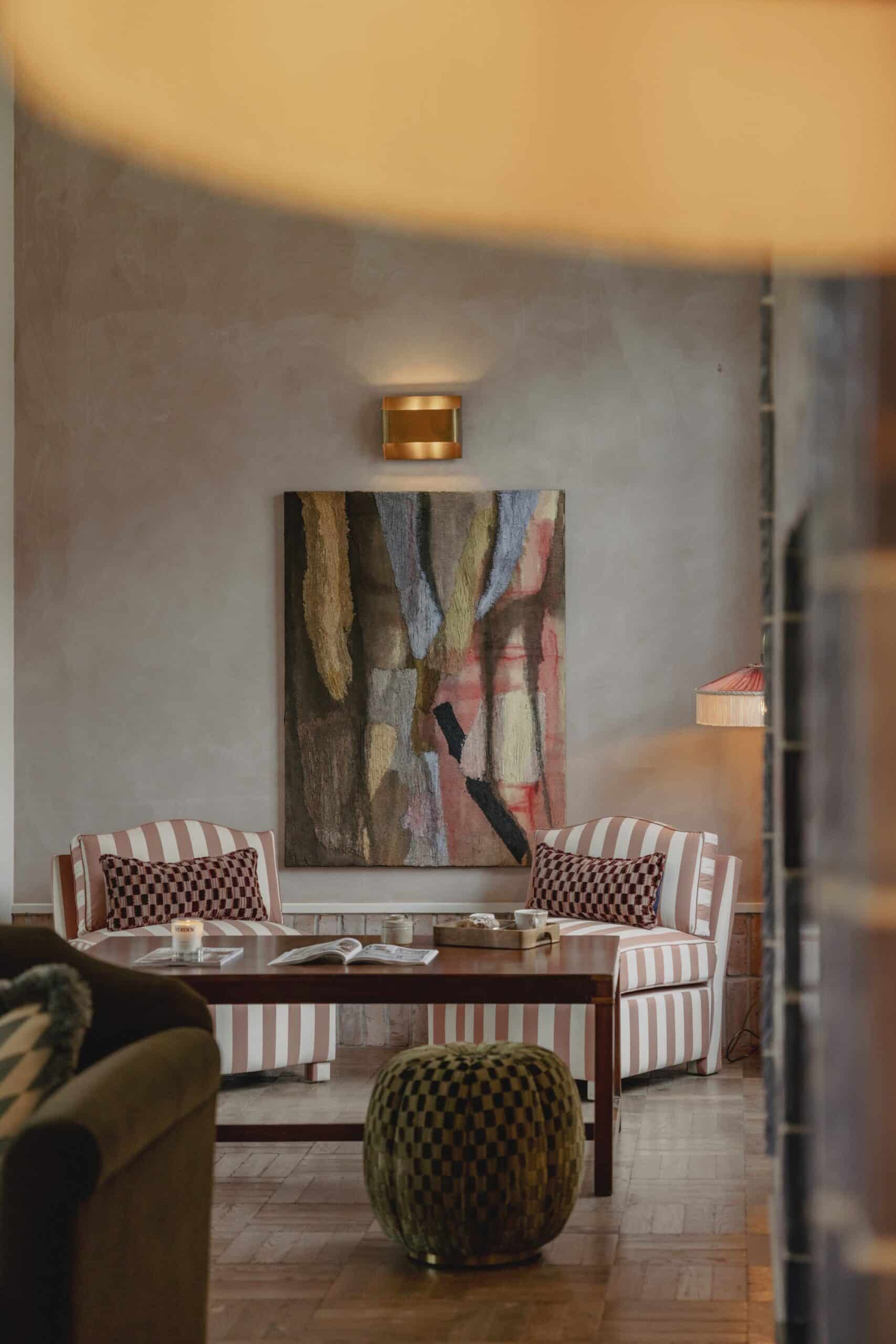 Cozy sitting area with striped chairs, a wooden table, abstract art, and soft lighting.