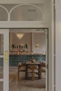 Modern dining area with wooden table and chairs in front of a bar with green tiles and drinks.