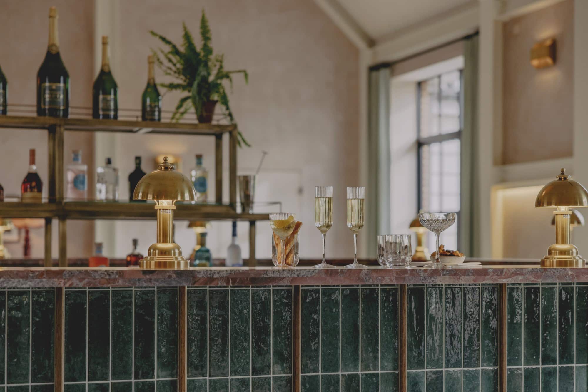 A stylish bar counter with drinks, snacks, and gold lamps in a cozy setting.