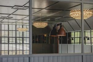 Chandeliers and lamps reflected in large windows and mirrors inside a modern, bright room.