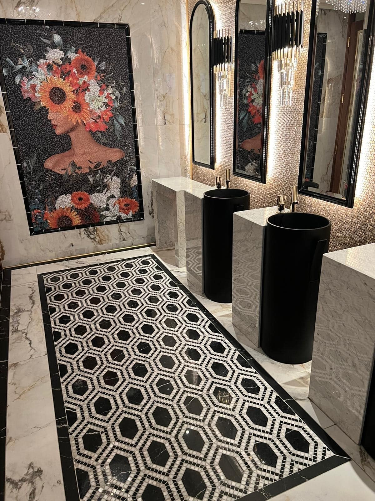 Elegant restroom with black sinks, mosaic floor, large mirrors, and floral art on the wall.