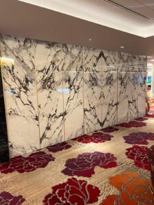 Marble wall with black veining and floral-patterned carpet in an indoor setting.