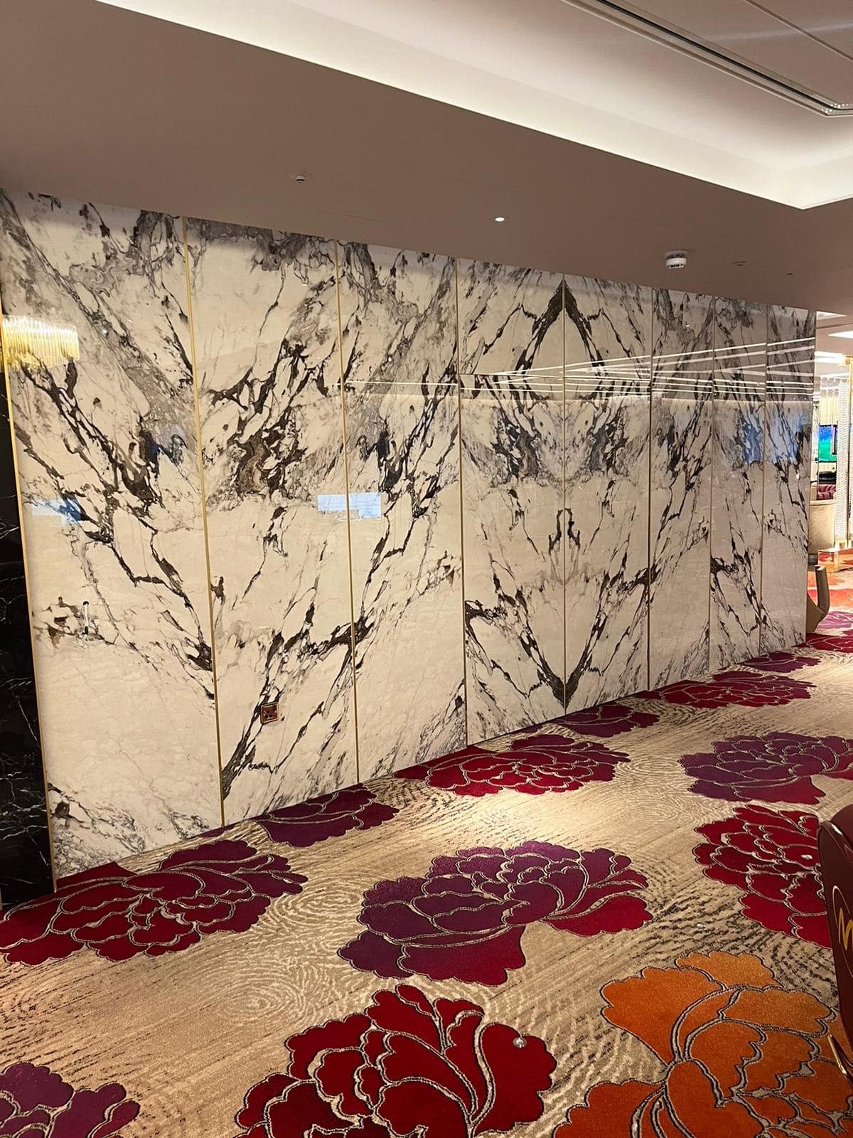 Marble wall with black veining and floral-patterned carpet in an indoor setting.
