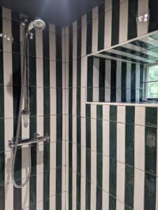 Shower with green and white vertical striped tiles and a wall mirror.