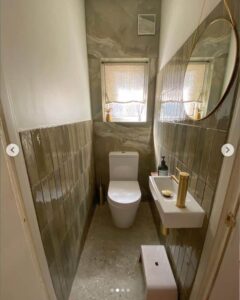 Small modern bathroom with a toilet, sink, mirror, and window.