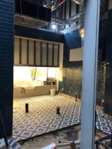 Room under construction with tiled floor and walls, pipes exposed, and equipment scattered around.