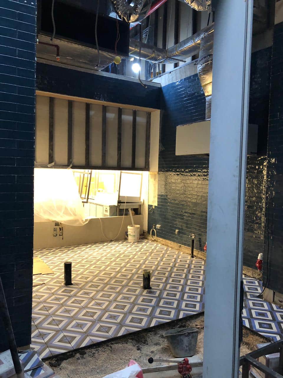 Room under construction with tiled floor and walls, pipes exposed, and equipment scattered around.