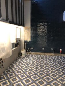 Room under construction with patterned tile floor and dark tiled wall.