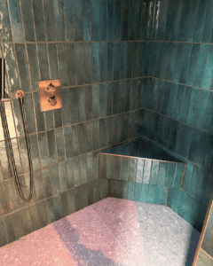 Shower with greenish-blue tiles, a built-in triangle bench, and a wall-mounted shower head.
