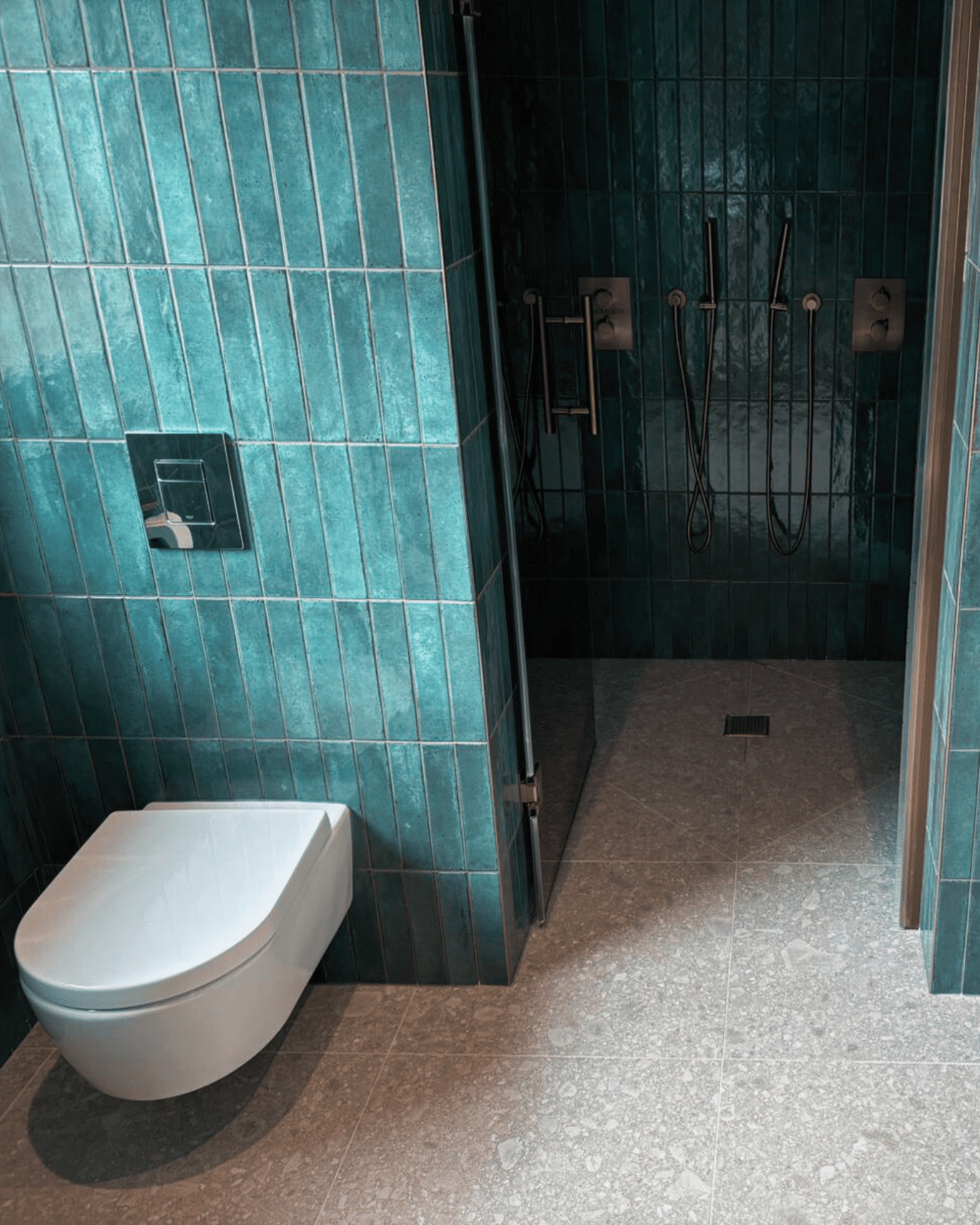 Modern bathroom with teal wall tiles, a wall-mounted toilet, and a walk-in shower.