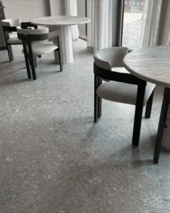 Round tables with modern chairs on a gray tile floor near large windows.