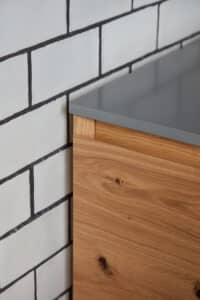 Wood cabinet with gray countertop next to a white tiled wall.