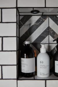 Shampoo and soap bottles on a tiled shower shelf with black and white herringbone background.