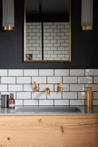 Modern bathroom with white subway tiles, gold fixtures, a mirror, and wooden vanity.