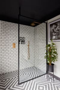 Modern shower with white subway tiles, black trim, a potted plant, and geometric-patterned floor.