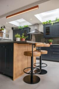 Modern kitchen with a wooden island, bar stools, skylights, and green plants on the countertops.