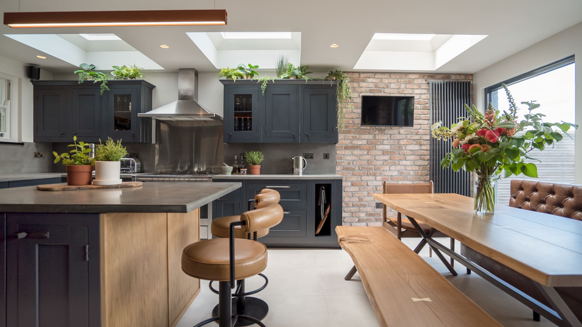 Modern kitchen with dark cabinets, island seating, dining table, skylights, and indoor plants.