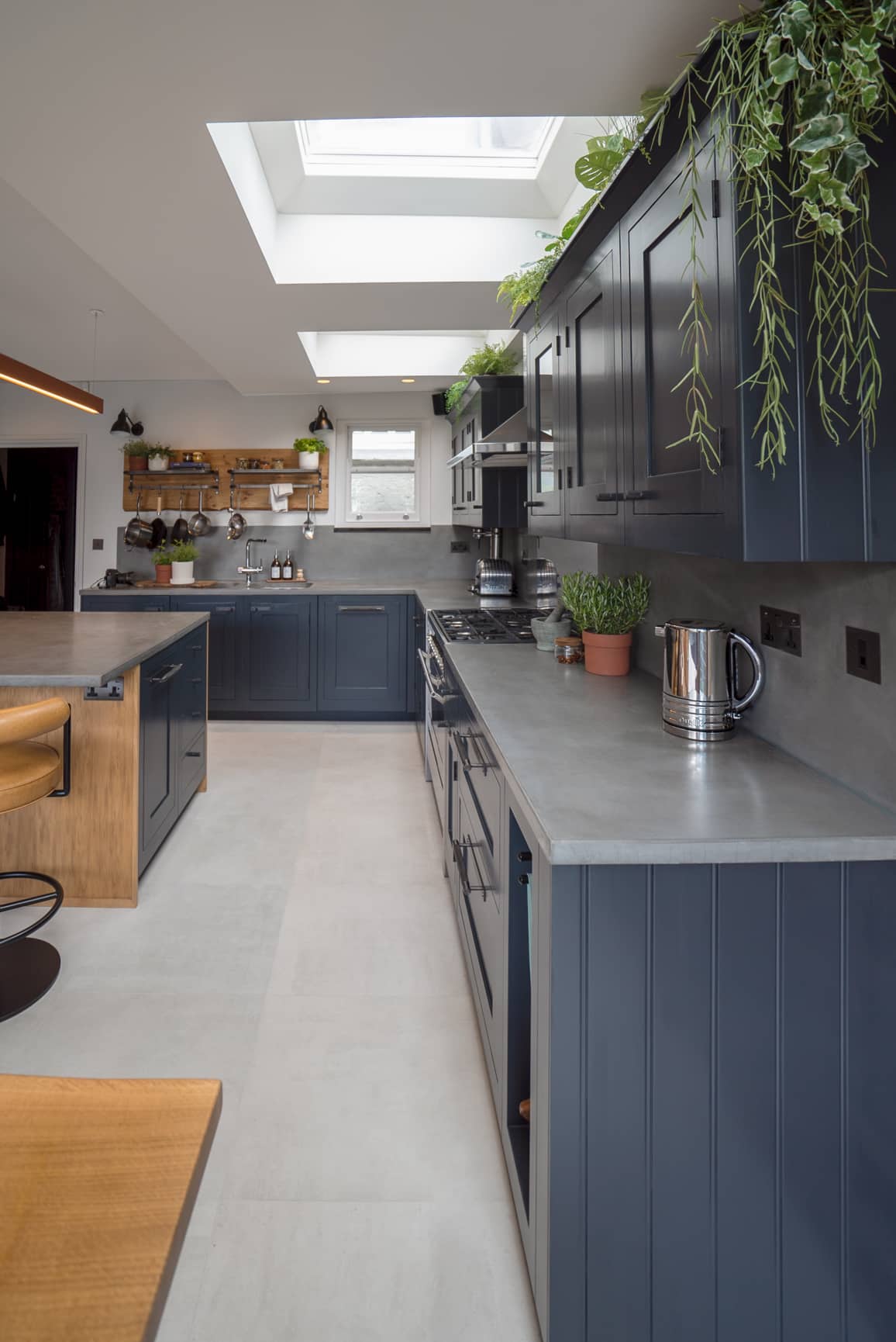 Modern kitchen with blue cabinets, skylights, hanging plants, and stainless steel appliances.