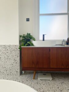 Modern bathroom with terrazzo walls, a wooden vanity, white sink, and a green plant by the window.
