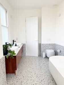 Modern bathroom with terrazzo floor, a bathtub, sink, toilet, and wooden vanity.