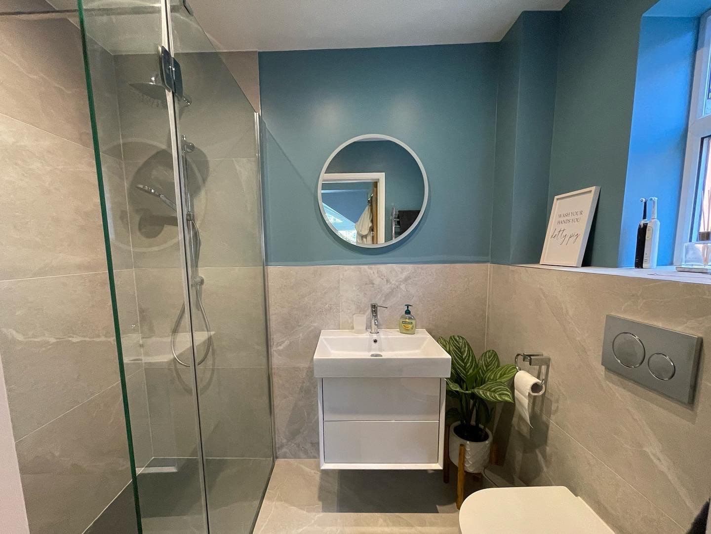 Modern bathroom with a glass shower, round mirror, sink, and toilet.