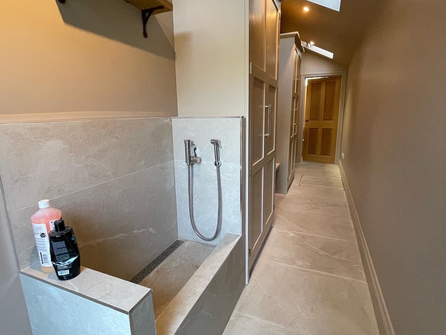 Narrow bathroom with a tiled shower area, handheld showerhead, and bottles on the ledge.