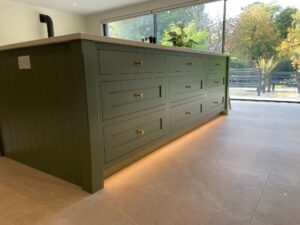 Green kitchen island with drawers, under-cabinet lighting, and large windows in the background.