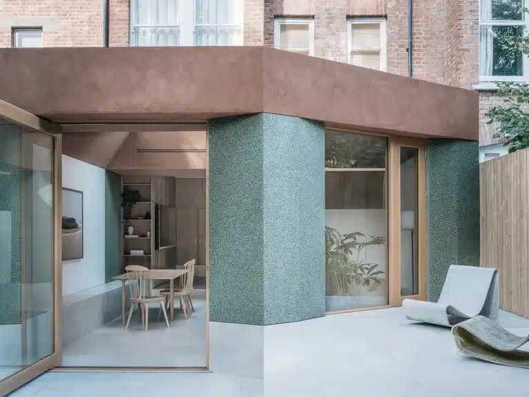 Modern house exterior with large windows, patio chairs, and a minimalist outdoor seating area.